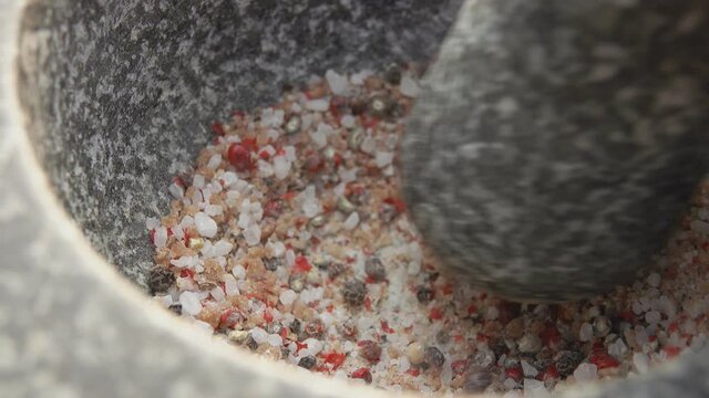 Pestle is grinding a mix of spices, peppers and sea salt in the grey stone mortar
