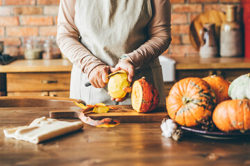 Female hands with knife chopping pumpkin on cutting board. Preparing autumn vegetables.