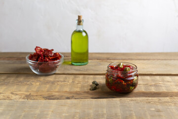 Sun-dried tomatoes in a glass jar with spices, capers and olive oil on a wooden table. Copy space. Horizontal orientation.