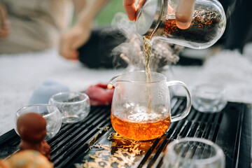 The process of brewing tea. Tea evaporates when pouring it into the kettle. Tea ceremony on the street on a sunny morning, a wonderful atmosphere.