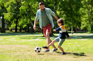 family, fatherhood and people concept - happy father and little son with ball playing soccer at summer park - obrazy, fototapety, plakaty