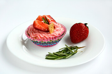 Cupcake with pink cream and strawberries on a white plate close-up