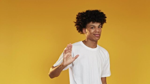 Like gesture. Bad job. Disappointed black guy in white t-shirt showing thumbs down and crossing hands looking at camera isolated on orange copy space. Disapproval sign. Wrong way