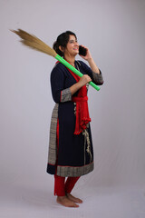 Young Indian woman or house wife using cellphone while holding broomstick in hand.