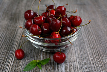 Juicy berries of a sweet cherry lie in a glass vase on a wooden table