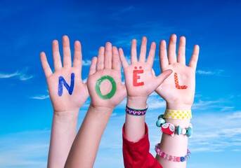 Children Hands Building Colorful French Word Noel Means Christmas. Blue Sky As Background