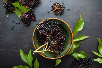 Raw ripe elderberry in a bowl standing on a dark table