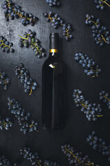 Wine in a bottle lying on a dark background decorated with bunches of grapes