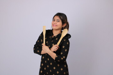 Beautiful Indian girl or woman or home maker holding serving spoon or kitchen ware in hand.