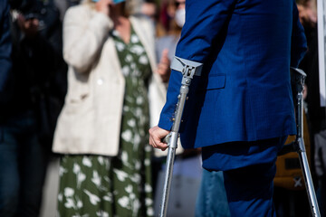 A disabled person with one leg in a strict suit walks on crutches.