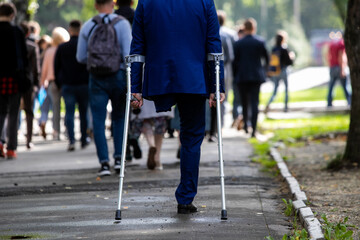 A disabled person with one leg in a strict suit walks on crutches.