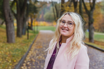 A beautiful blonde girl in a pink coat walks in the Park