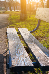 Old wooden park bench close-up on blurred green nature background. Relax backdrop for text sign, copy space banner with vertical orientation. Morning sun lights, calm tranquil wallpaper