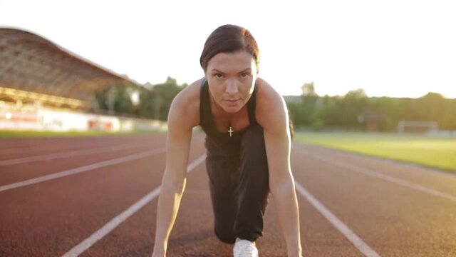 Serious female runner in crouch start position preparing for race on running track at stadium 