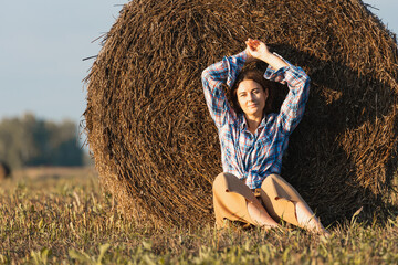 Happy lifestyle concept - beautiful woman enjoying the beautiful weather and posing against the haystack, field