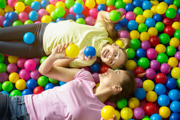 Fototapeta na wymiar Cute girl and her mum lying together in ball pit at indoor playground, top view