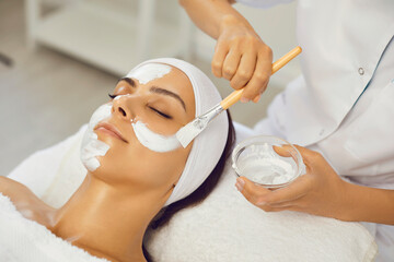 Cosmetologist smearing mask for serene woman in beauty spa salon