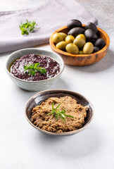 Tapenade - paste made from olives. Bowls with spreadable black and green olive cream on concrete background.