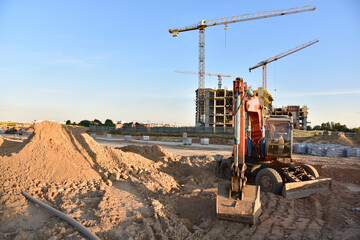 Wheel excavator during road work at construction site. Screeding gravel for laying asphalt and installing borders and curbs on road. Tower crane in action.  Road roller for paving works