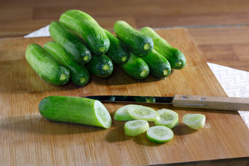Pile of Fresh cucumber and cucumber slices on wooden cutting board and wooden table