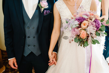The bride and groom with a wedding bouquet, holding on hands and standing on wedding ceremony of...