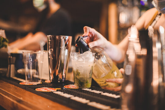 Dettaglio mani che preparano una bevanda alcolica posta sopra un bancone in legno di un locale estivo serale