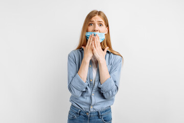 Shocked, surprised young woman in a medical protective mask on her face, surprised covers her mouth with her hand, on a white background