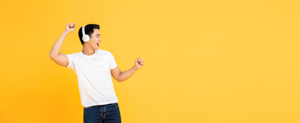 Young handsome Asian man wearing headphones listening to music and dancing on yellow banner background