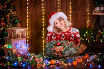 Fototapeta na wymiar Woman making handmade christmas wreath on table. Christmas decoration and composition. Girl dressed in christmas design sweater prepare christmas wreath for holiday.