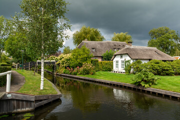 Fototapeta na wymiar Giethoorn, The Netherlands - August 28, 2020: Houses with thatched roof along the canal