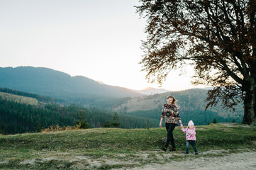Fototapeta na wymiar Mom with daughter walking in mountains during sunset. Autumn evening.