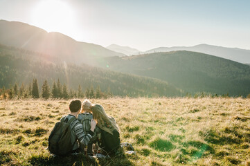 Happy Hipster family: mom, dad, daughter with backpack enjoying sunset on peak of foggy mountain. Tourists traveler on background view mockup. Hikers looking sunlight in trip in country Europe.