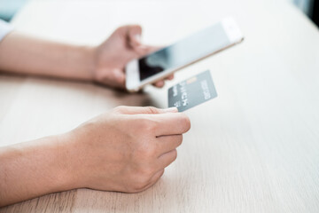 The businesswoman's hand is holding a credit card and using a smartphone for online shopping and internet payment in the office
