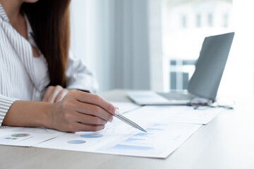 Asian female accountant sits at their desks and calculates financial graphs showing results about their investments, plan a successful business growth process