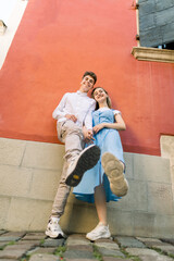 Happy crazy funny couple in summer casual clothes, having fun outdoors in the city, posing to camera, laughing and raising their legs in sneakers up