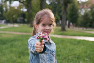 little cute girl holding a bouquet of clover flowers in her hands, street portrait in the park
