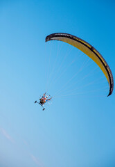 A paraglider with a yellow parachute against a clear blue sky.