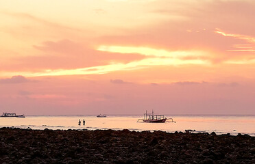 Young people fishing in a traditional way, next to a catamaran in Gili Trawangan, Lombok, Indonesia
