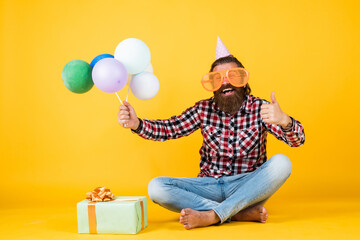 holiday celebration. bearded mature man celebrate birthday party. cheerful man in bday hat hold holiday balloons. gifts and presents concept. have a happy holiday. party time. happy birthday to you