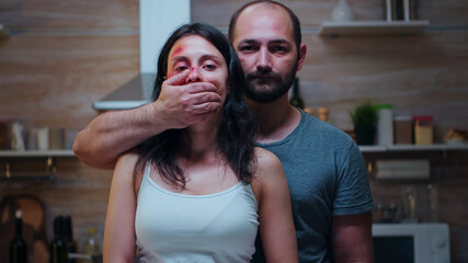 Man covering the woman's mouth looking at the camera. Violent aggressive man abusing injuring...