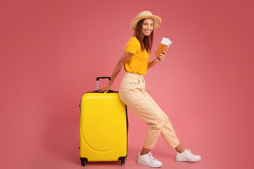 Smiling young woman in summer clothes leaning on luggage