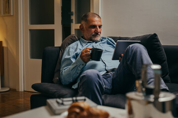 middle aged man sitting sofa using tablet computer at home