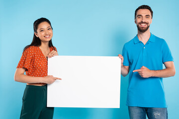 asian woman in red blouse and man in polo t-shirt pointing with fingers at blank placard on blue