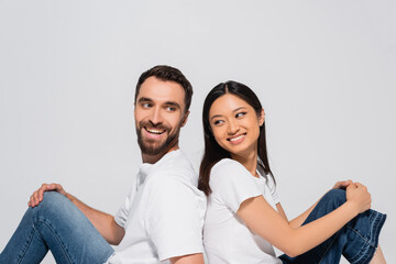 brunette asian woman and bearded man in white t-shirts sitting back to back isolated on white