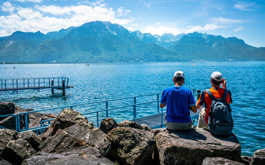 Two unrecognizable tourists admiring the view on Lake Geneva and the Alps on Montreux shoreline in Switzerland