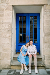 Obraz na płótnie Canvas Lovely date on the street. Happy hipster young couple, handsome man with his attractive girlfriend in blue dress, hugging outdoors in the city, posing near beautiful vintage blue door
