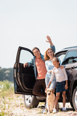 Selective focus of man waving hand near family with golden retriever and auto outdoors