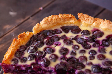 Edge of rustic shortbread pie with blueberries in sour cream filling on a wooden background with piece cut off