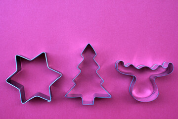 Steel Christmas tree, star, and deer shaped cookie cutters on red background with copy space.