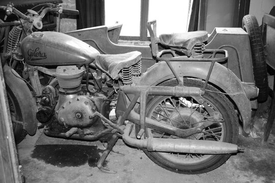 Oldtimer Gilera motorbike abandoned in barn in tuscany black and white dust.